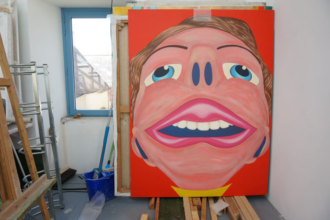 Peinture dans l'atelier de Benoît Andro qui représente une grande tête avec une grande bouche sur fond rouge vermillon.