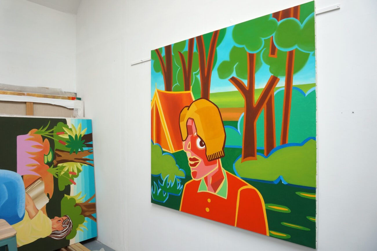 Peinture accrochée au mur dans l'atelier de l'artiste peintre Benoît Andro qui représente un personnage en plein-air devant un paysage de sous-bois. Ce personnage a l'air de camper là.