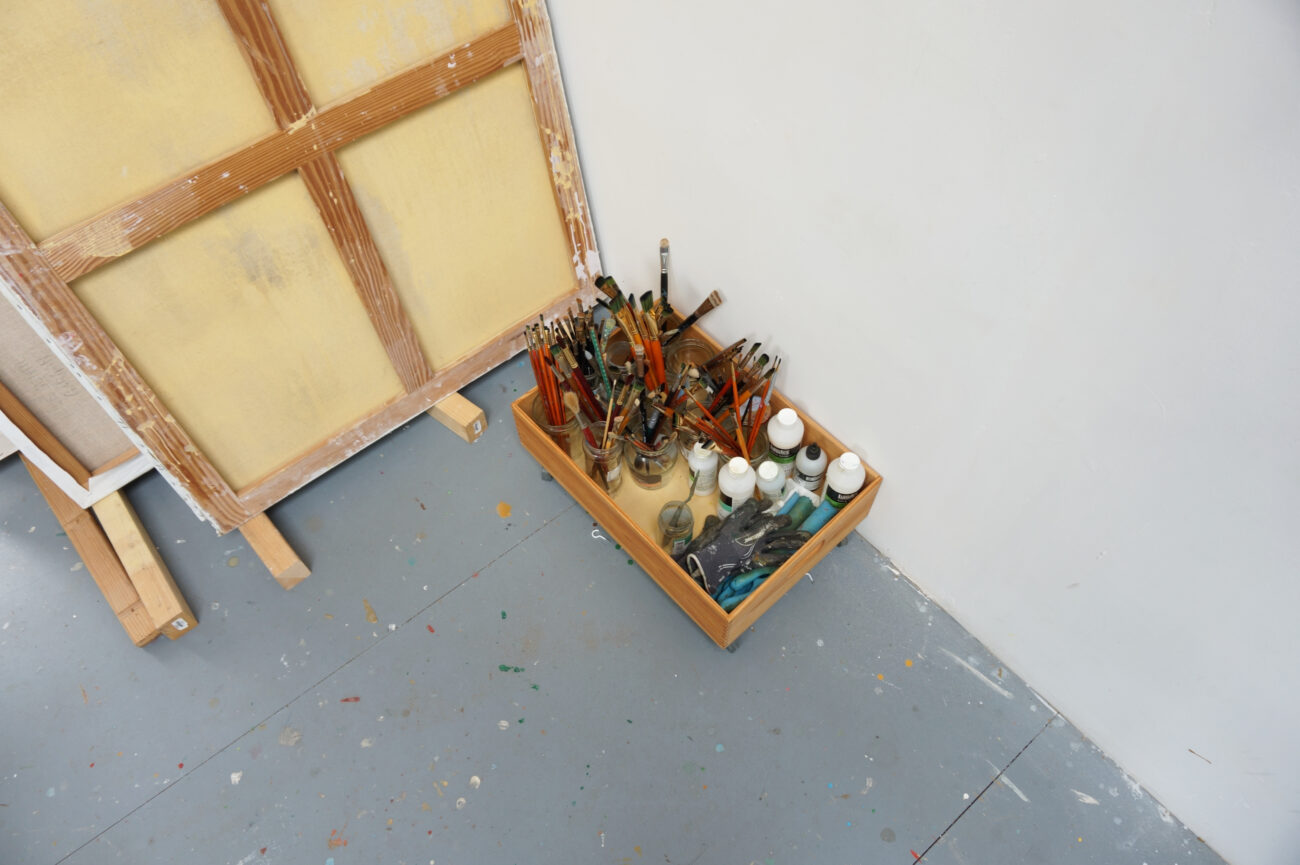 Dans l'atelier de benoit andro pinceaux et mediums dans une boîte à roulette devant une toile inversée
