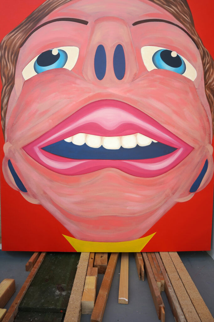 Peinture dans l'atelier de Benoît Andro qui représente une grande tête avec une grande bouche sur fond rouge vermillon.