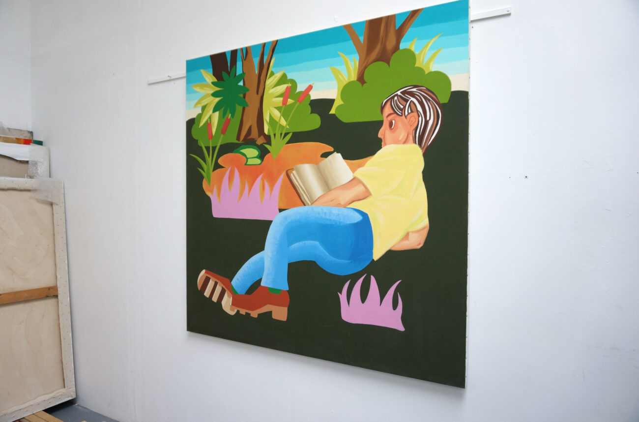 Peinture accrochée au mur dans l'atelier de l'artiste peintre Benoît Andro qui représente un personnage en train de lire un livre en plein-air.